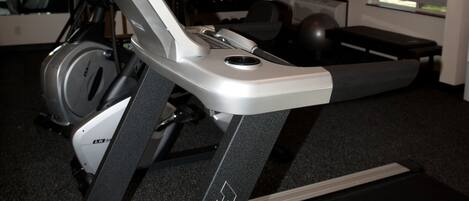 Un gimnasio con equipo de ejercicio que incluye cintas de correr, bicicletas estáticas y pesas.