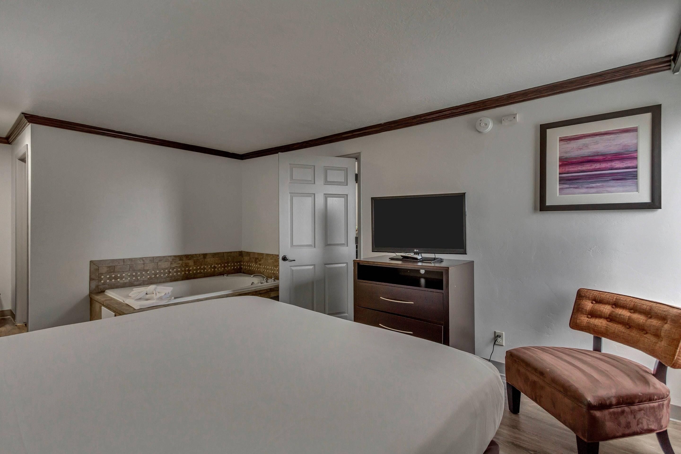 A bedroom with a bed, a wooden chair, a dresser, a television, and a door.