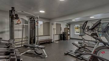 Un gimnasio con máquinas de cardio, equipo de levantamiento de pesas y bancos.