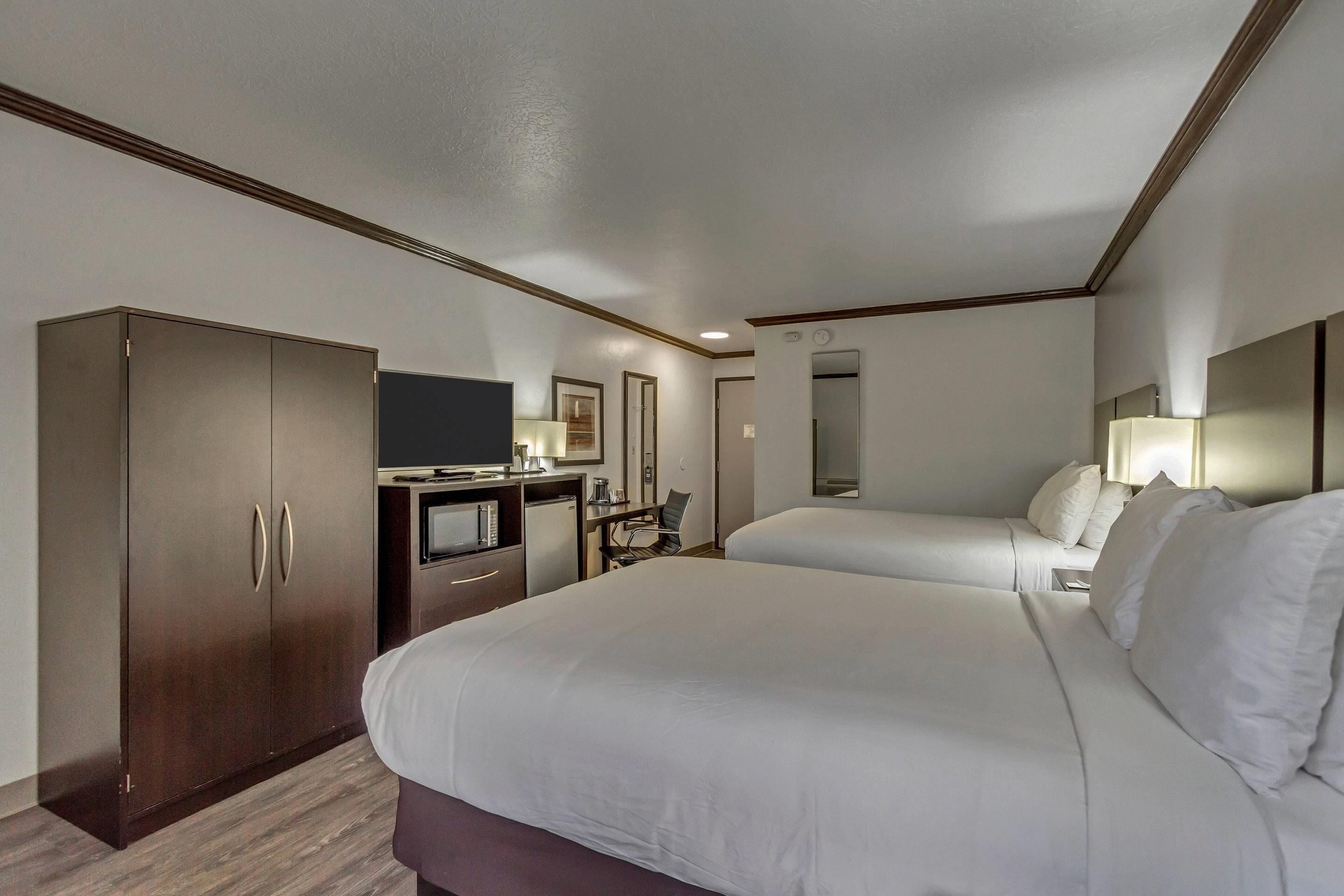 A hotel room with a large bed, a desk with a computer, a television, and a wardrobe.