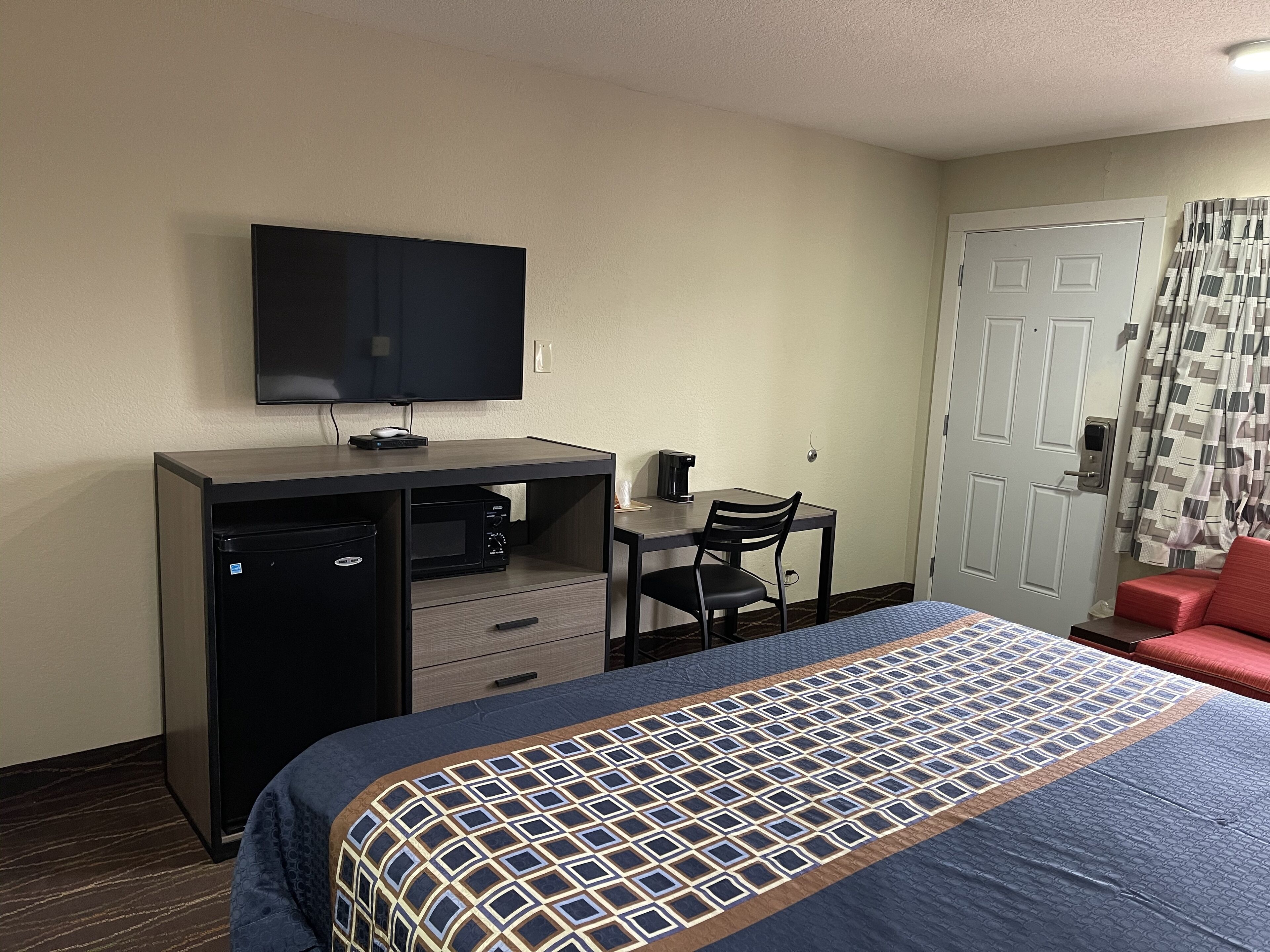 A hotel room with a bed, a desk with a computer and a television, a chair, and a door with a curtain.