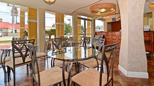 A dining area with a glass table and chairs, a wooden reception desk, and large windows with a view of the street.