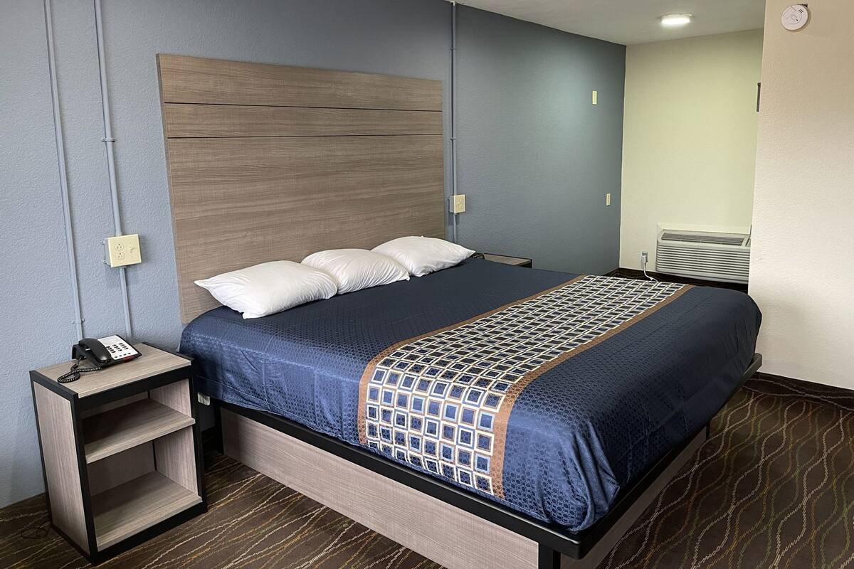 A hotel room with a bed, bedside table, and a wall-mounted heater.