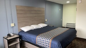 A hotel room with a bed, a bedside table, a power outlet, and a wall-mounted air conditioner.