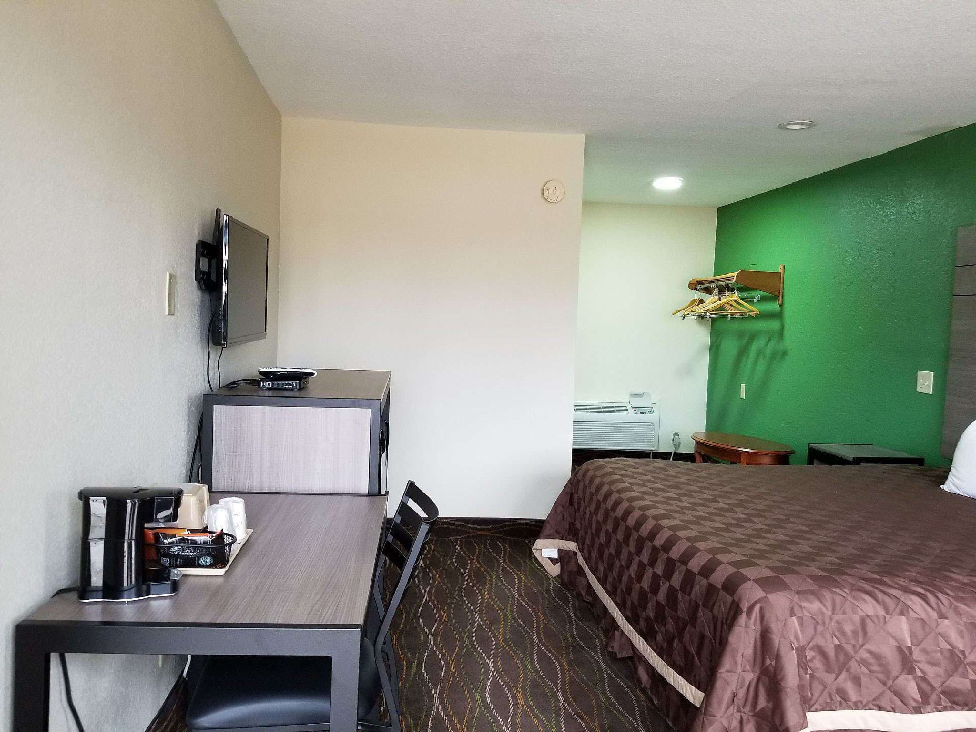 A hotel room with a bed, a desk with a computer, a TV, and a green wall.