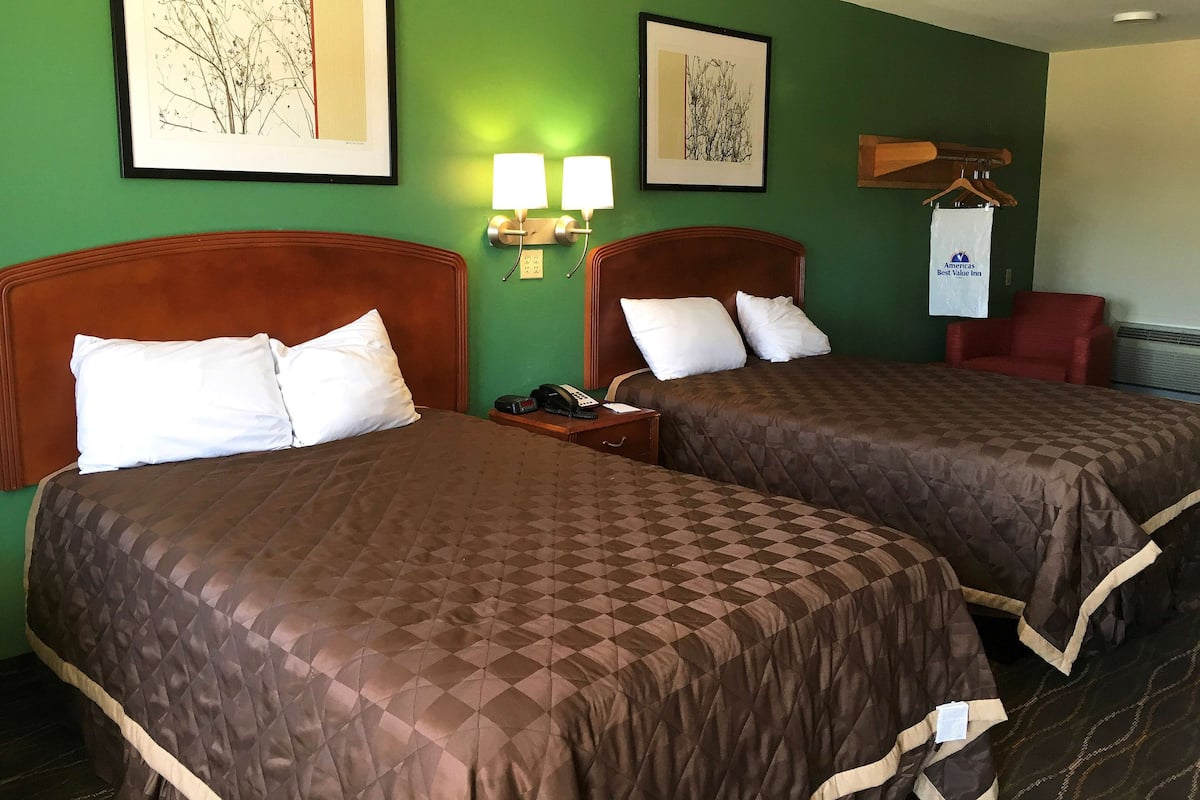 A hotel room with two beds, green walls, framed artwork, a red chair, and a white hanging sign.