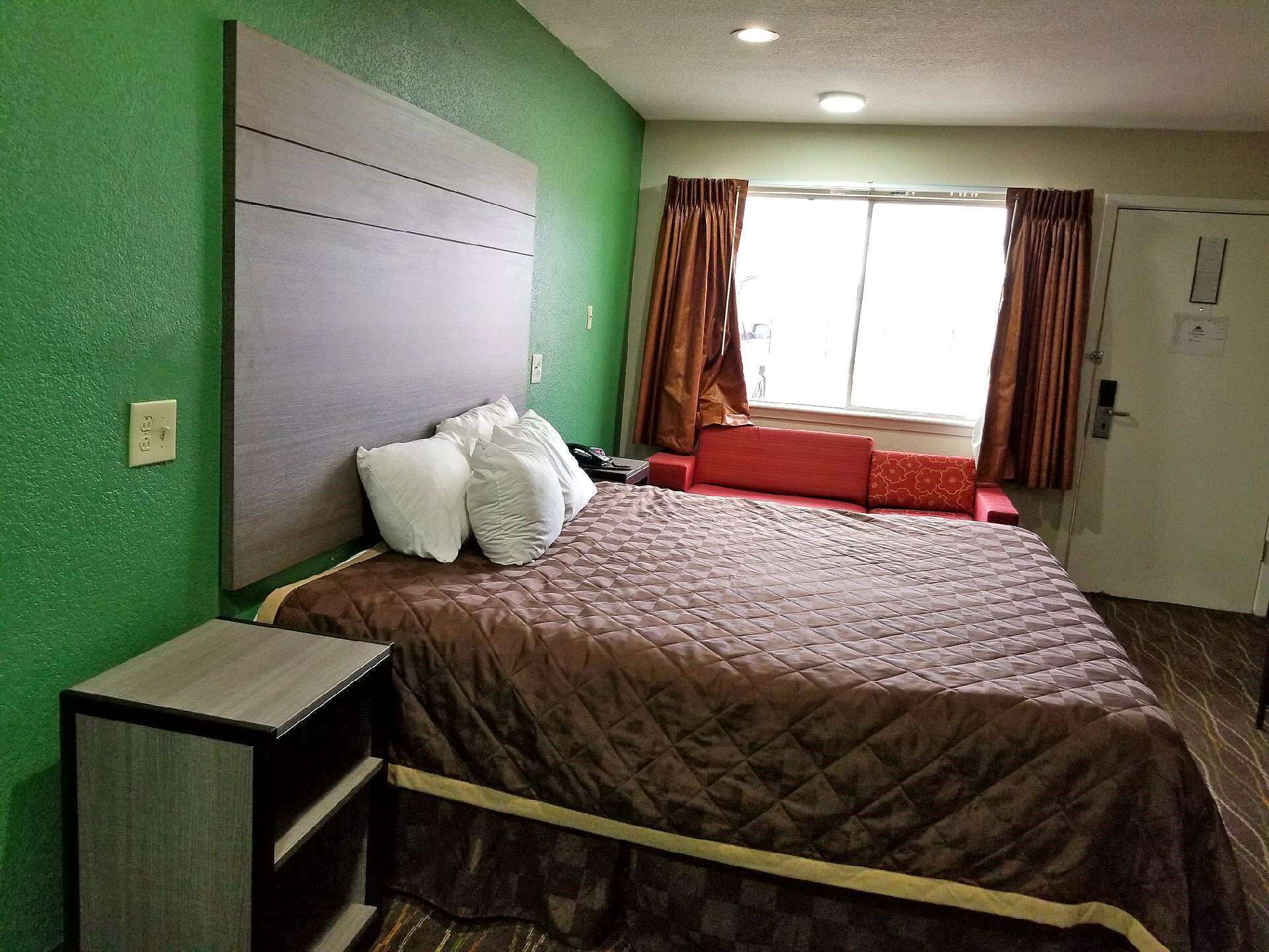 Una habitación de hotel con cama, mesita de noche, ventana con cortinas y puerta.
