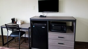 A compact workspace with a desk, chair, coffee maker, microwave, and a TV mounted on the wall.