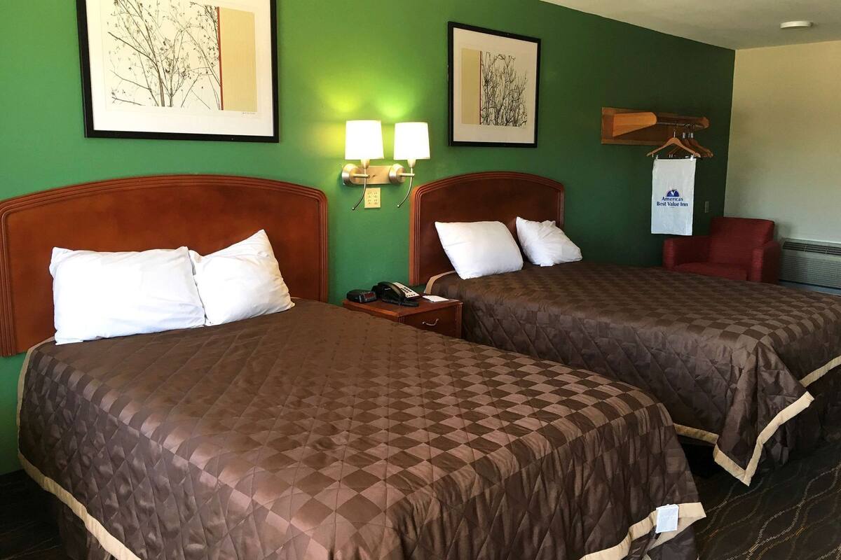 A hotel room with two beds, green walls, framed artwork, a nightstand with a phone, and a red chair.