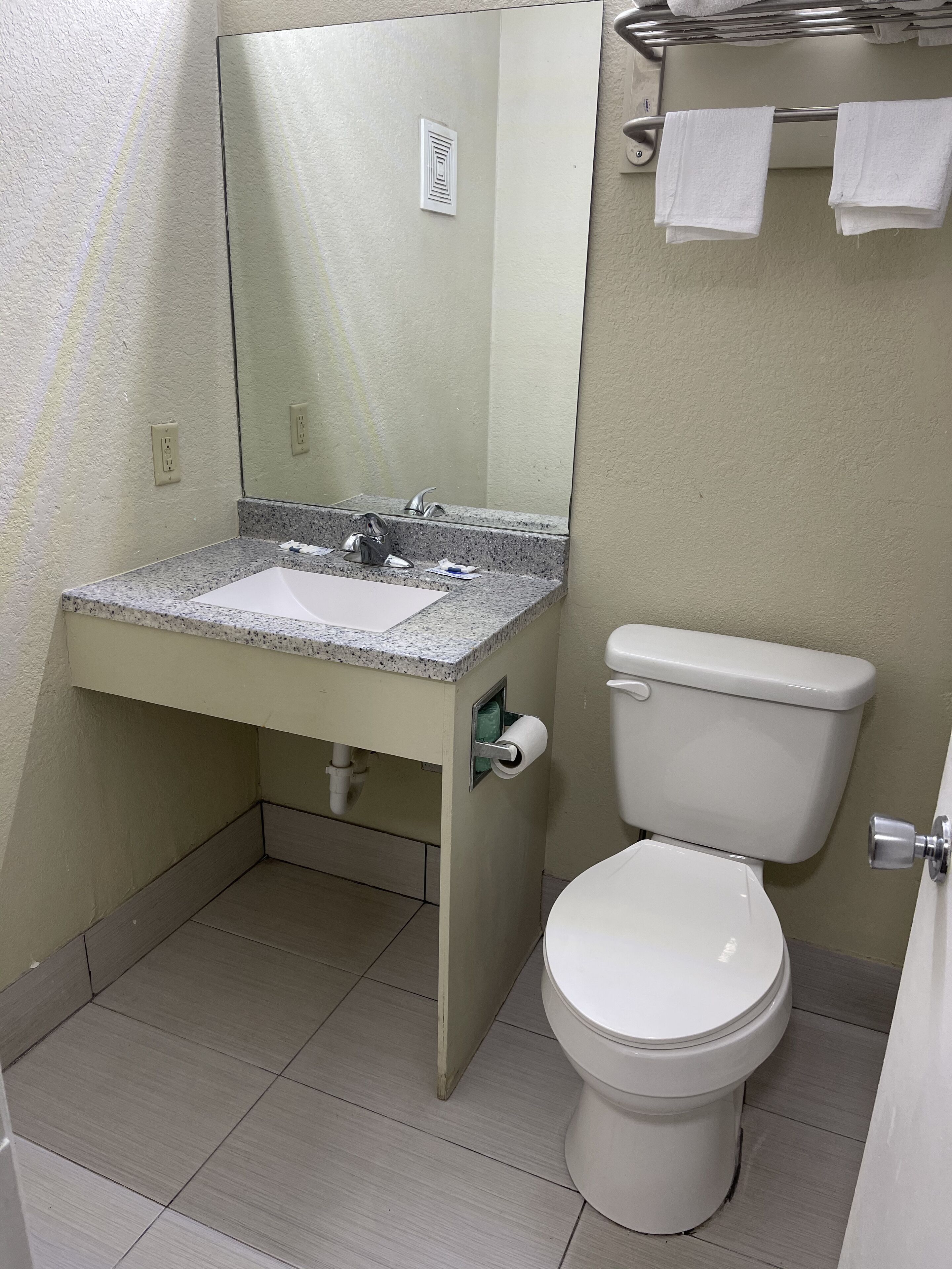 A bathroom with a sink, mirror, toilet, and towel rack.