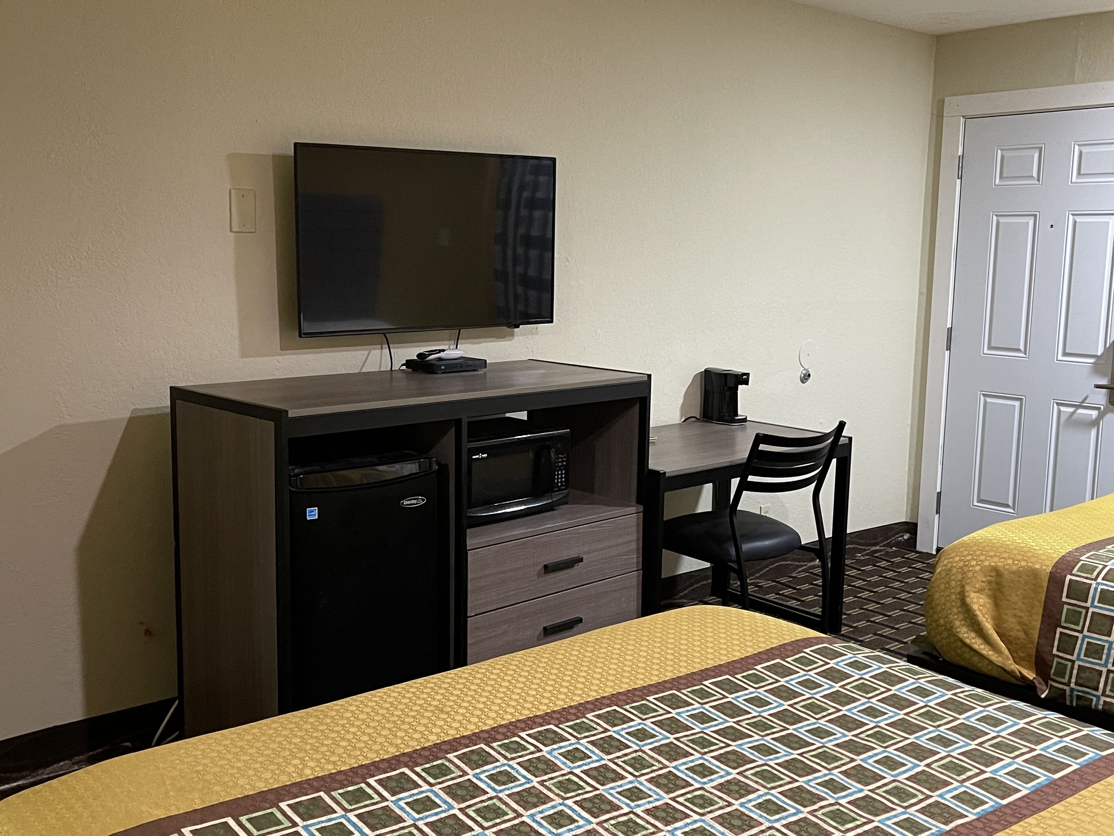 Ein Hotelzimmer mit Bett, Schreibtisch, Fernseher, Mikrowelle und Kaffeemaschine.
