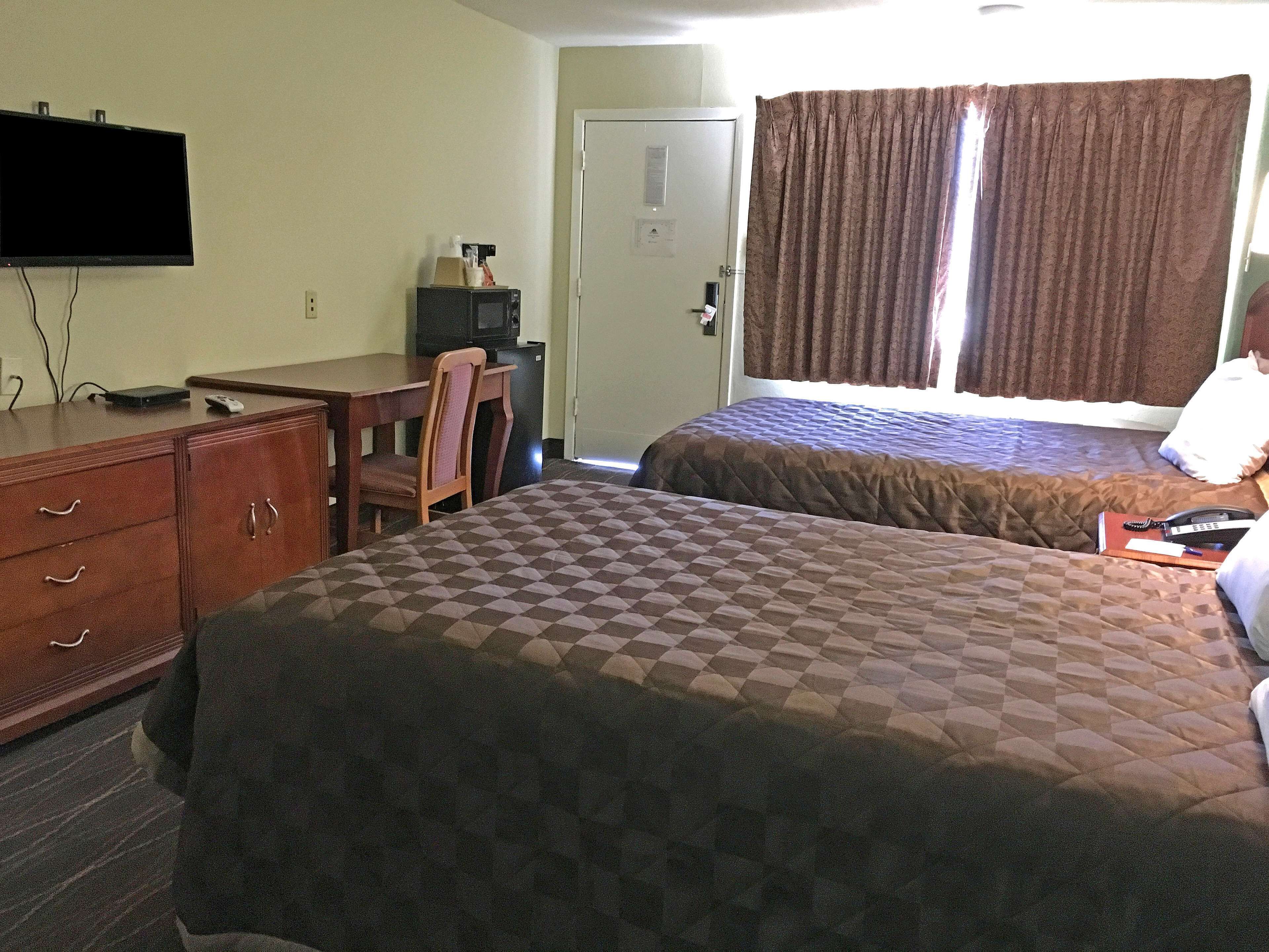 Habitación de hotel con dos camas, un escritorio, una silla, un televisor y una puerta.