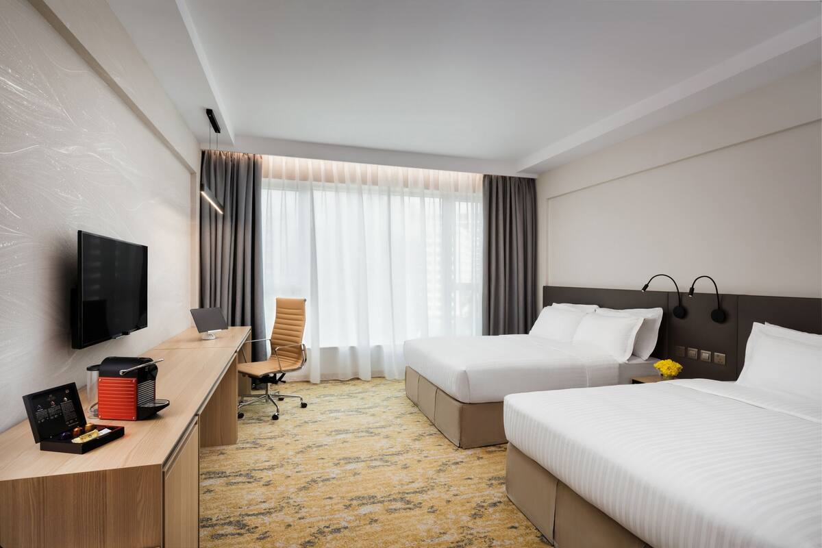 A hotel room with two beds, a desk with a computer, a TV, and a window with curtains.