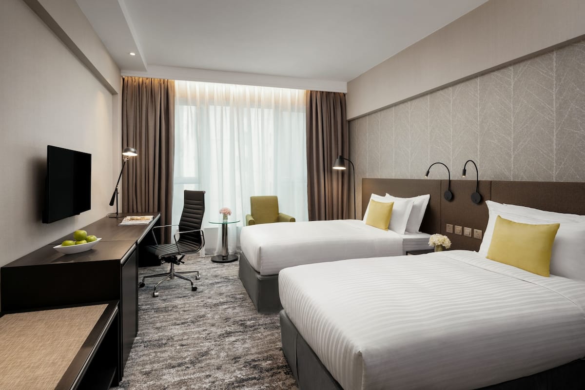 A hotel room with two beds, a desk, a TV, and a small table with a bowl of fruit.