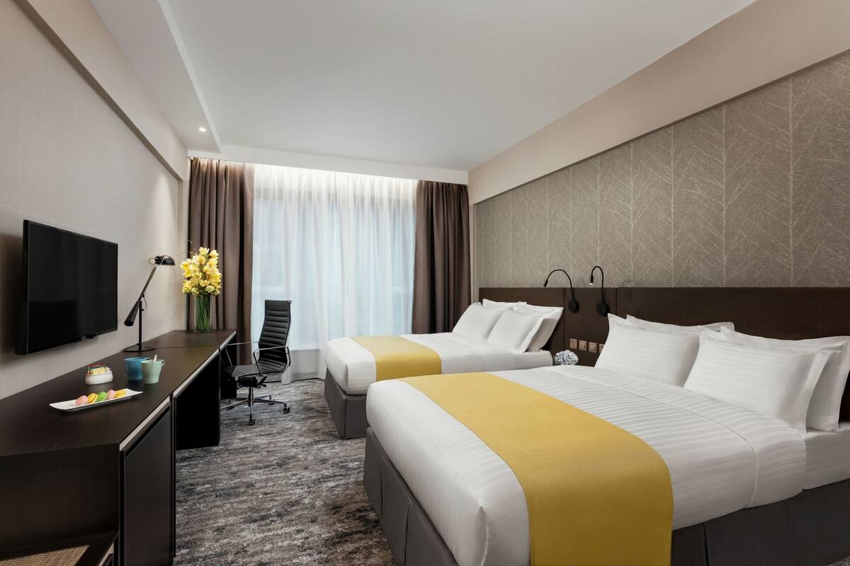 A hotel room with two beds, a desk, a TV, and a window with curtains.