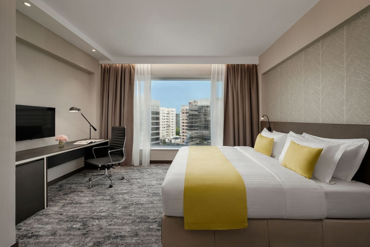 A hotel room with a large bed, a desk with a computer, a TV, and a view of buildings through the window.