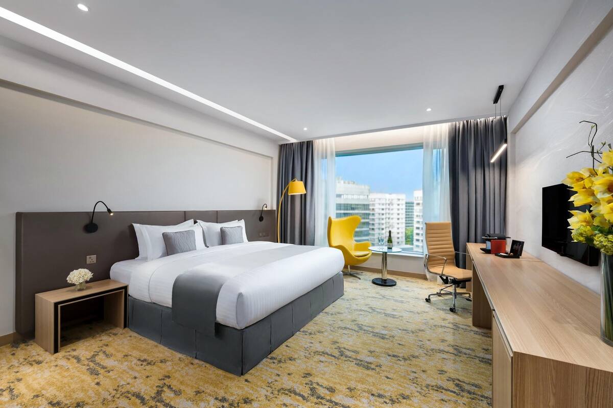 A modern hotel room with a large bed, a desk, a chair, and a view of the city.