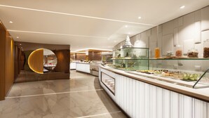 Un moderno vestíbulo de hotel con piso de mármol, un mostrador de recepción curvo y una vitrina de vidrio con distintos productos alimenticios.