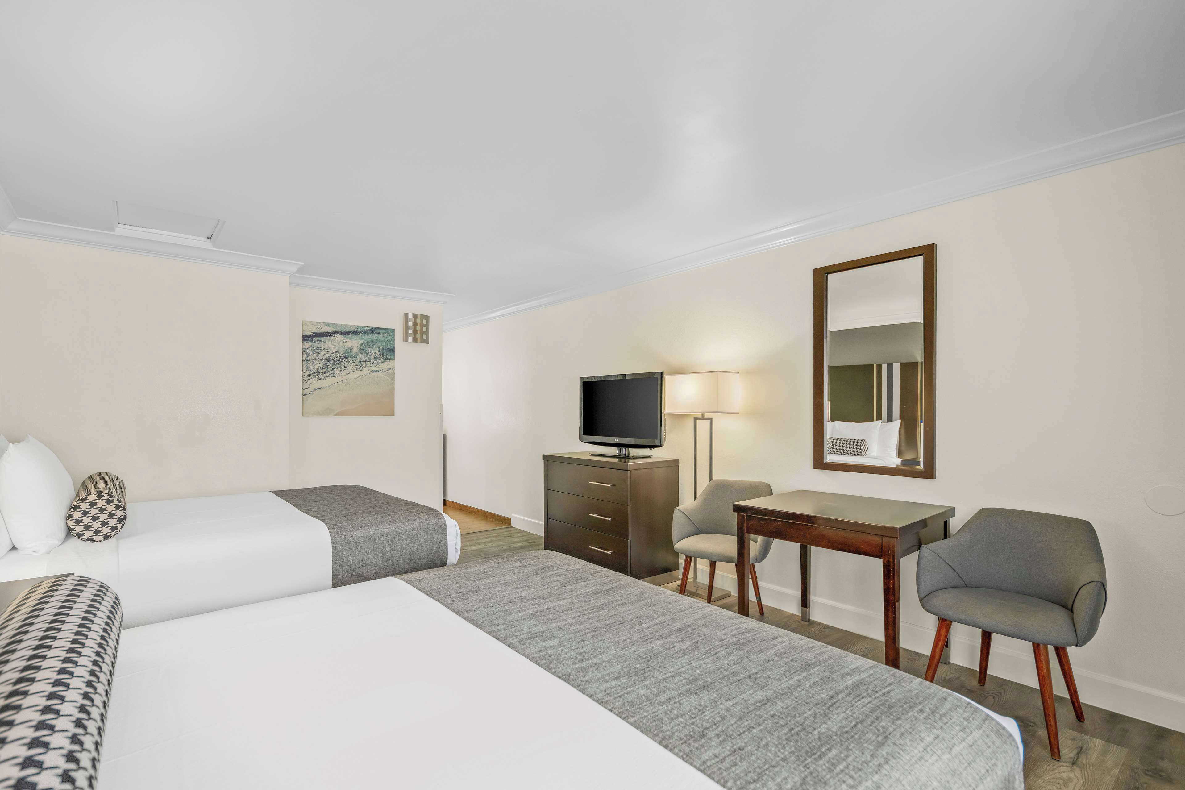 A hotel room with two beds, a desk, a chair, a television, and a mirror.