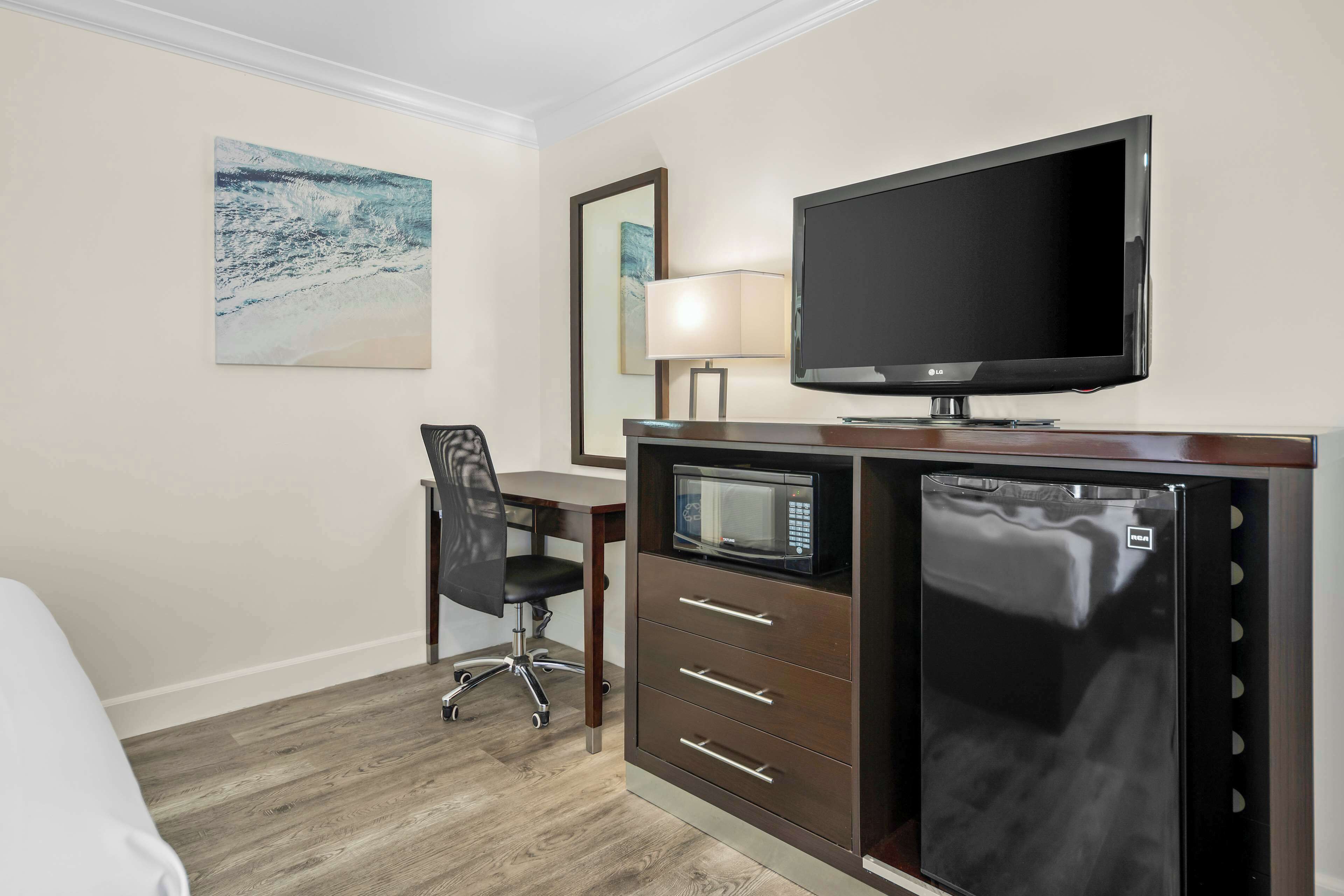 A hotel room with a bed, a desk with a chair, a television, a microwave, and a refrigerator.
