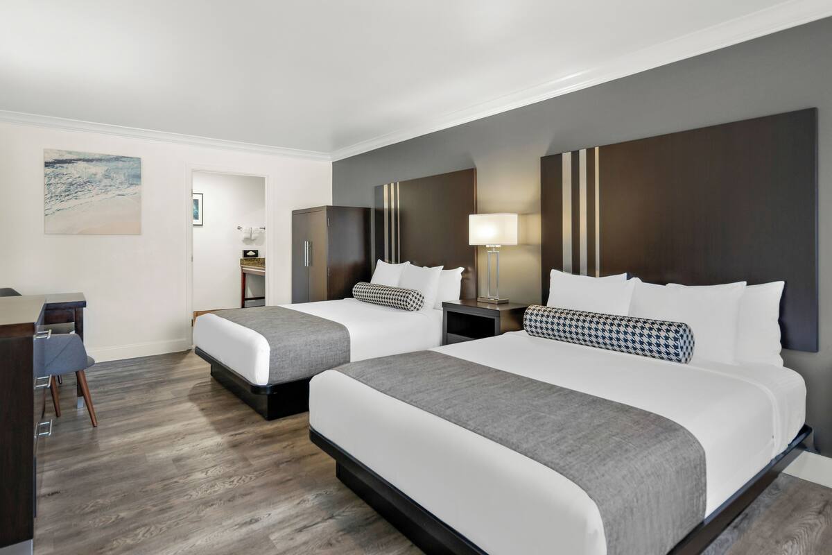 A hotel room with two beds, a desk, and a chair.