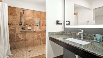 A bathroom with a shower, a sink, and a large mirror.