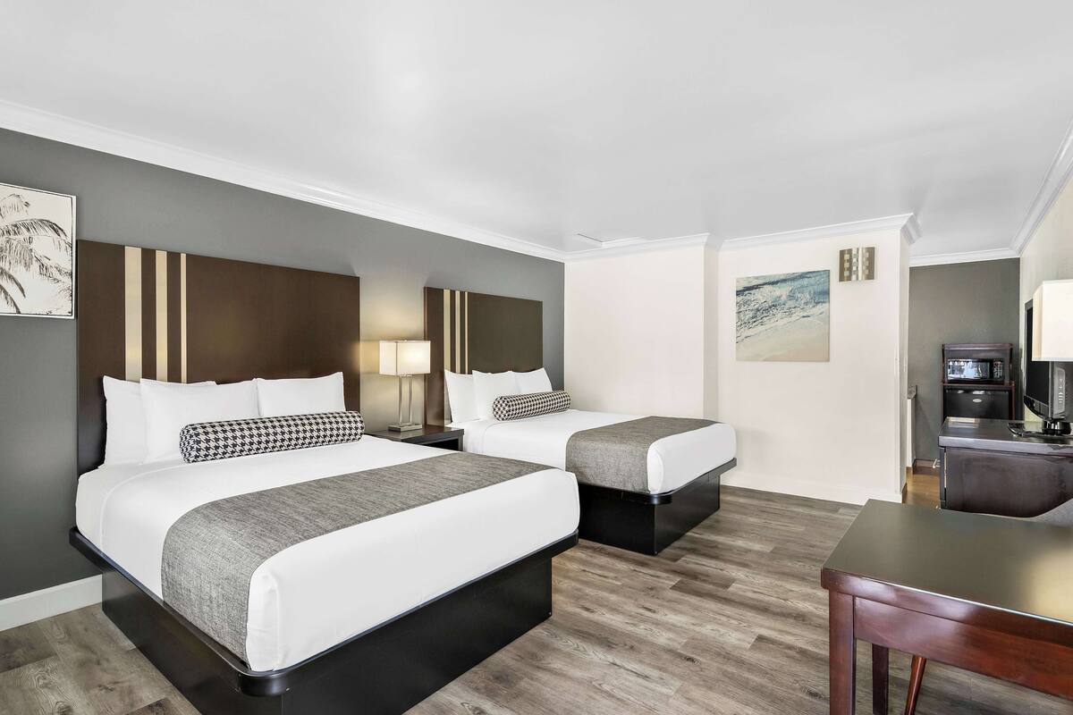 A hotel room with two beds, a desk, a microwave, and a TV.