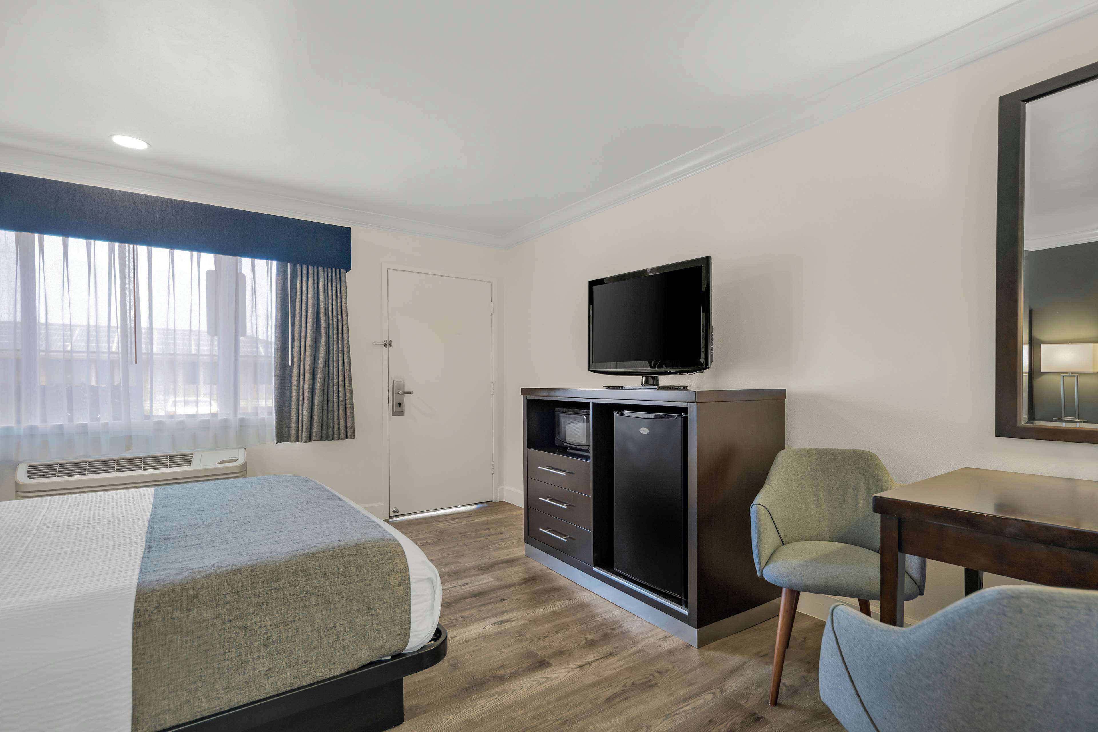 A hotel room with a bed, a desk, a chair, a television, and a wardrobe.