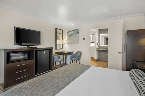 A hotel room with a bed, a desk with a chair, a television, a microwave, and a refrigerator.
