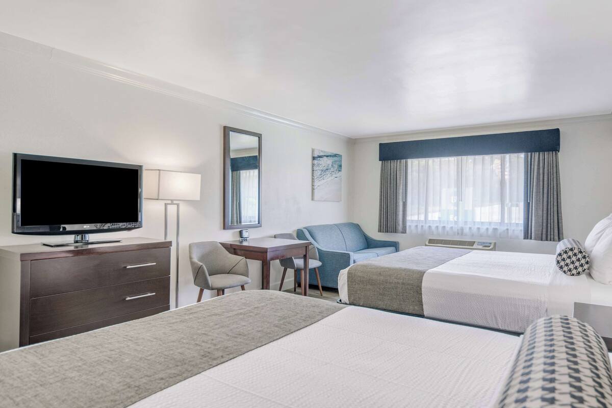 A hotel room with two beds, a desk, a chair, a television, and a window with curtains.