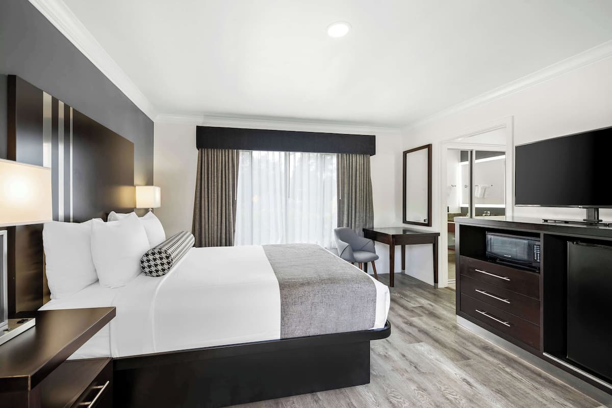 A hotel room with a bed, bedside table, lamp, desk, chair, and a TV.