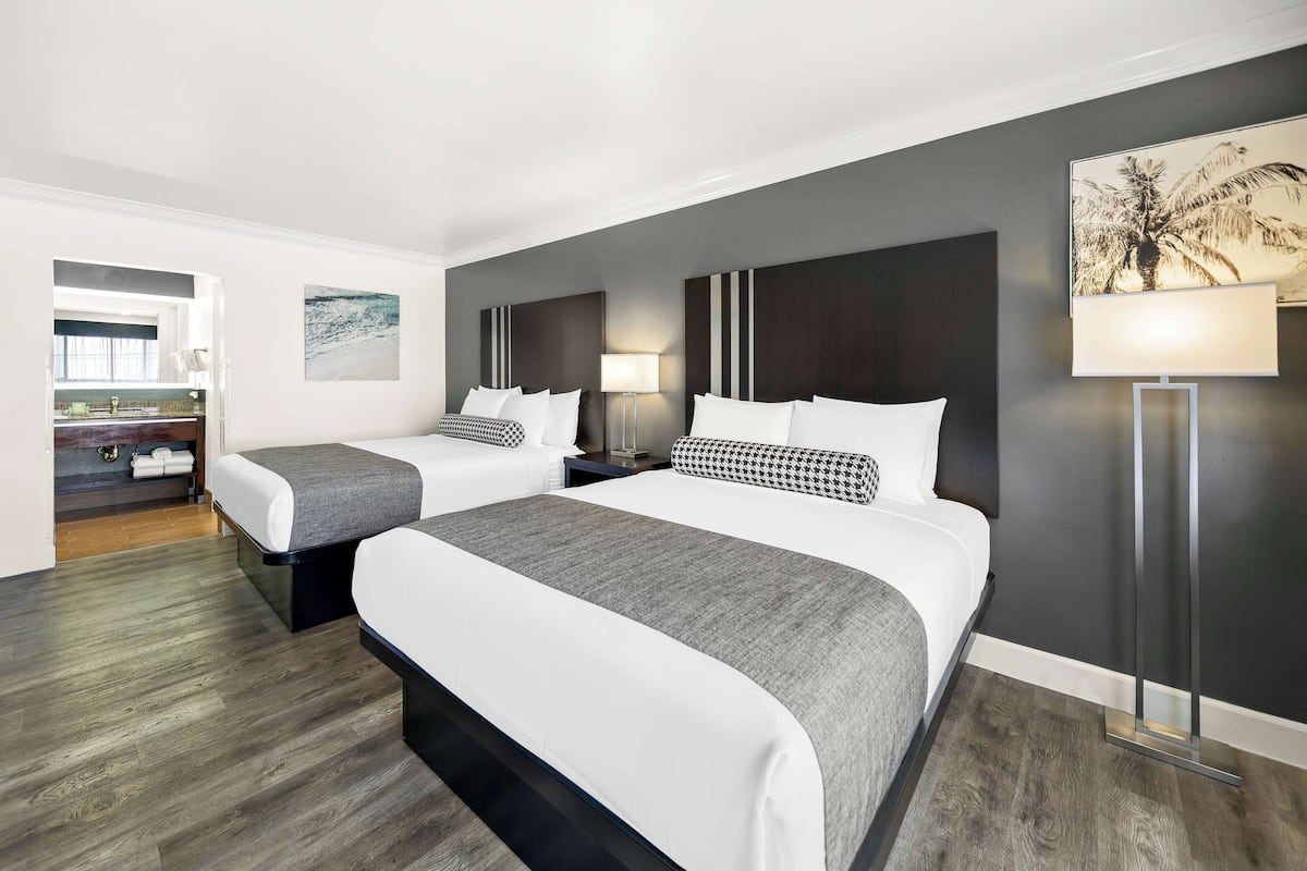 A hotel room with two beds, a nightstand, a lamp, and a painting on the wall.