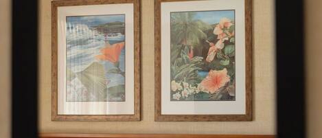 A hotel room with a bed, two framed paintings on the wall, and a wooden headboard.