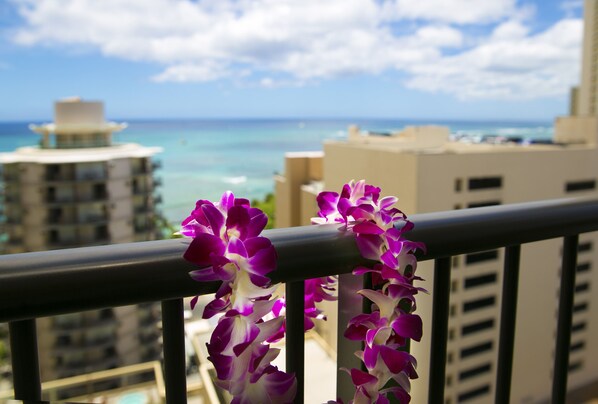 A balcony with purple flowers, a view of the ocean, and buildings in the background. - Waikiki Resort Hotel (Honolulu)