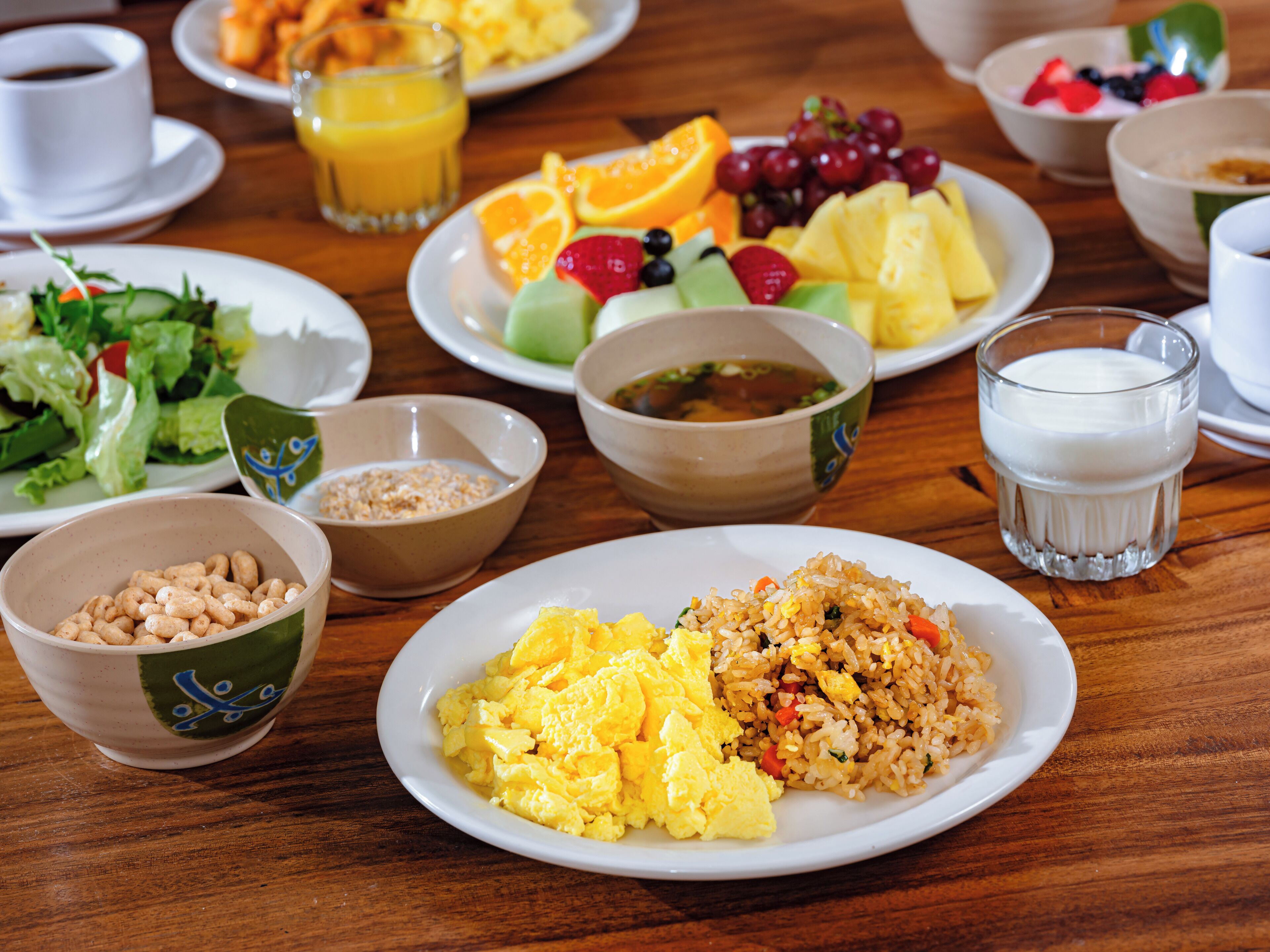 A breakfast table with various dishes including scrambled eggs, fried rice, and fruit.