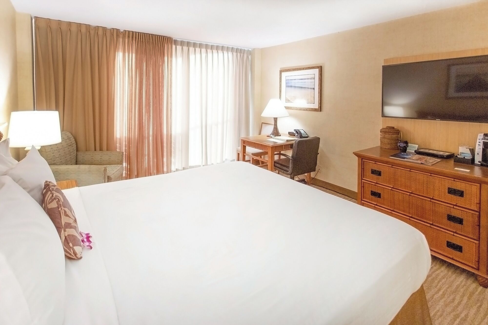 Habitación de hotel con una cama grande, un escritorio con lámpara, una silla, un televisor y un aparador de madera.