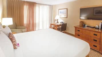 A hotel room with a large bed, a desk with a lamp, a chair, a television, and a wooden dresser.