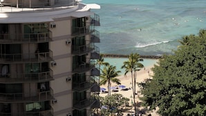 A high-rise hotel with multiple balconies overlooking a beach with clear turquoise water and a few boats. - Waikiki Resort Hotel (Honolulu)