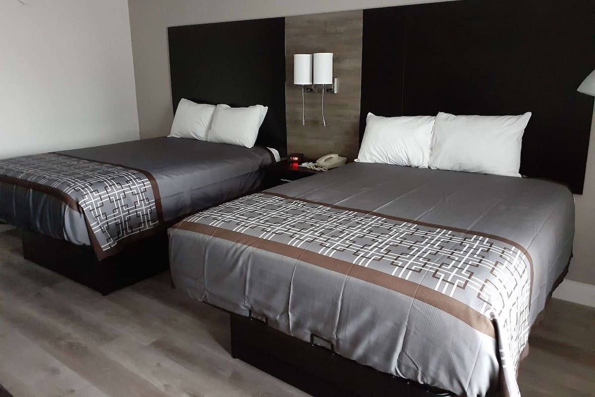 A hotel room with two beds, a nightstand with a phone, and a wall-mounted lamp.