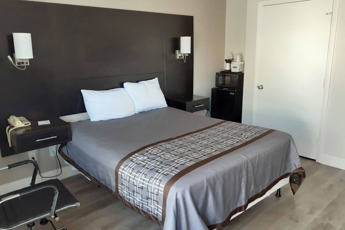 A hotel room with a bed, bedside tables, a desk with a chair, a microwave, and a door.