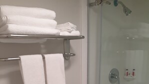 Un baño con ducha de vidrio, inodoro y estante con toallas dobladas.