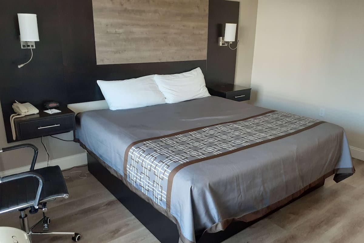 A hotel room with a bed, bedside tables, a desk with a chair, and a phone.