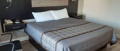 A hotel room with a bed, bedside tables, a desk with a chair, and a phone.