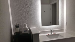 Un baño con pared blanca texturizada, un lavamanos blanco con grifo moderno y un espejo sobre el lavamanos.