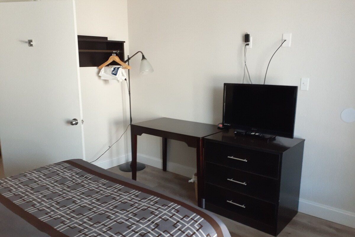 A bedroom with a bed, a desk, and a television.