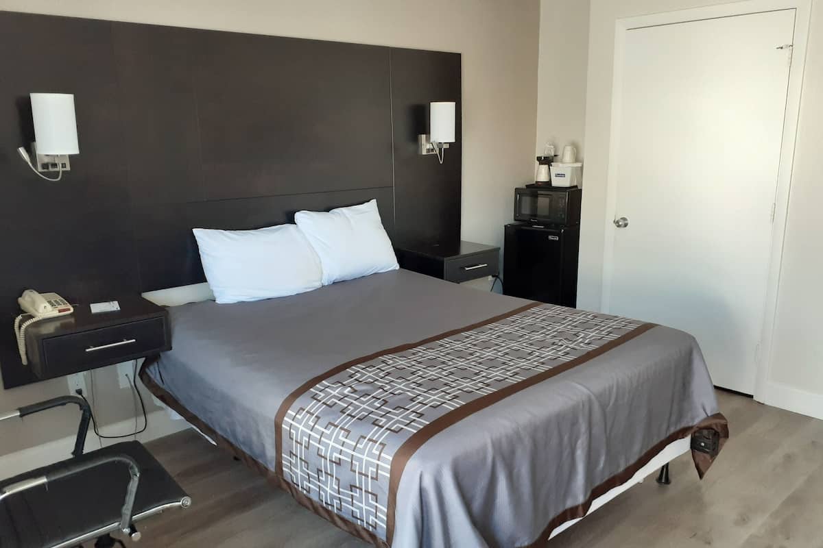 A hotel room with a large bed, bedside tables, a desk with a chair, a microwave, and a telephone.