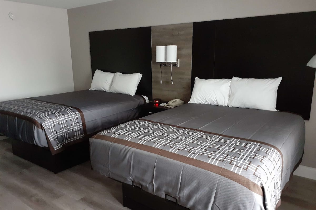 A hotel room with two beds, a nightstand, a telephone, and a wall-mounted light fixture.
