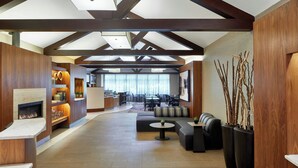 A spacious lobby with a fireplace, seating area, and a view of the dining area. - Courtyard by Marriott Rochester East/Penfield (Rochester)