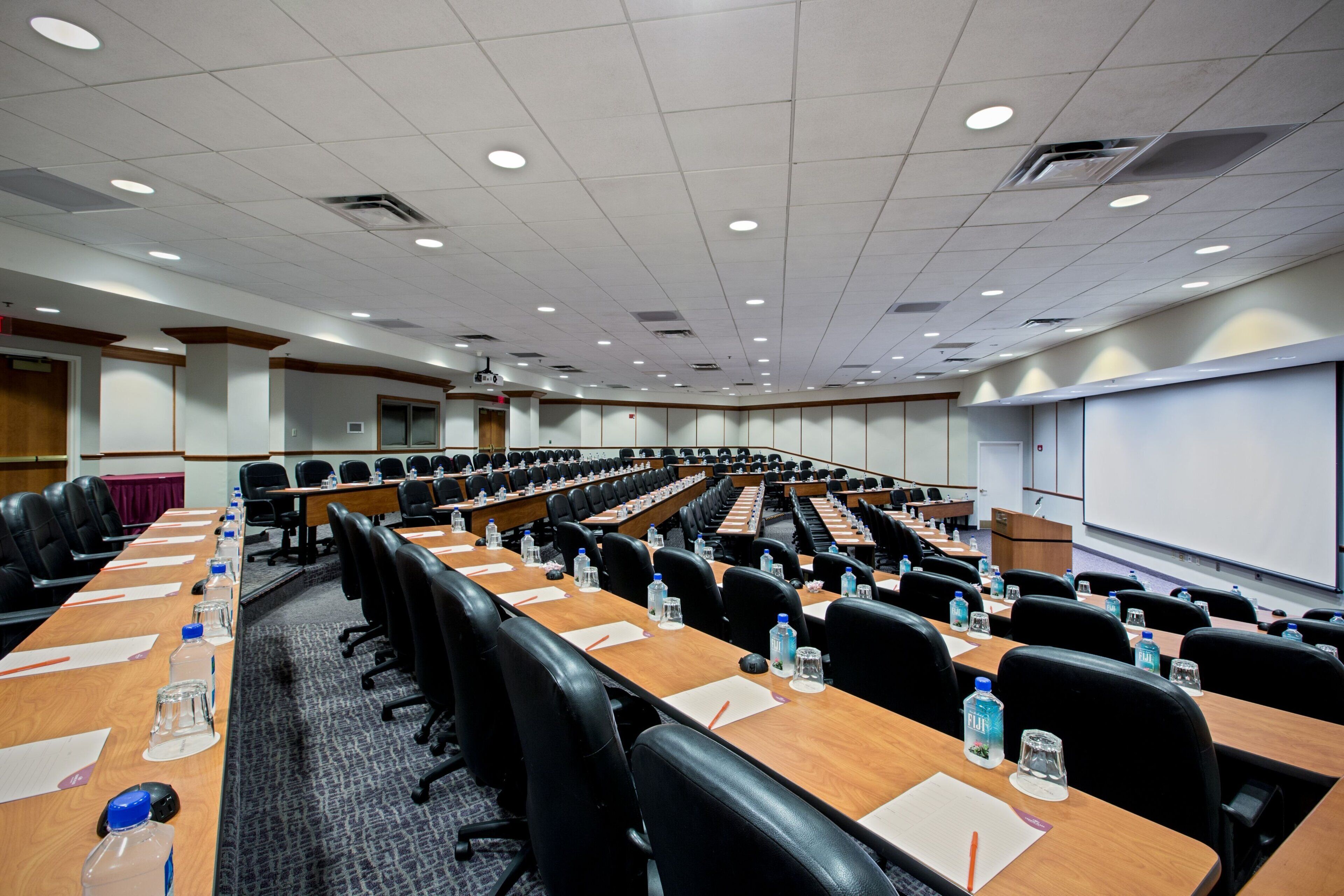Une salle de conférence équipée de longues tables, de chaises et d’un écran de projection.
