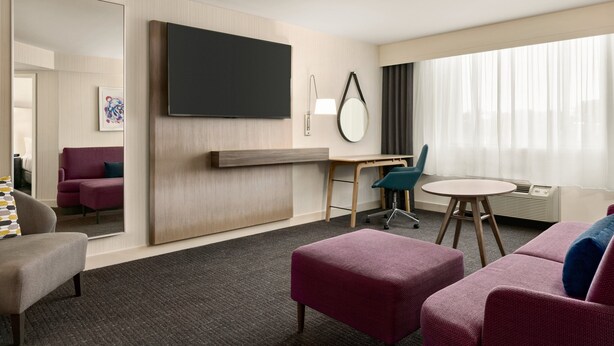 A hotel room with a large mirror, a flat-screen TV, a desk with a chair, a round table, and two sofas. - Crowne Plaza: Philadelphia - King of Prussia by IHG (King of Prussia)